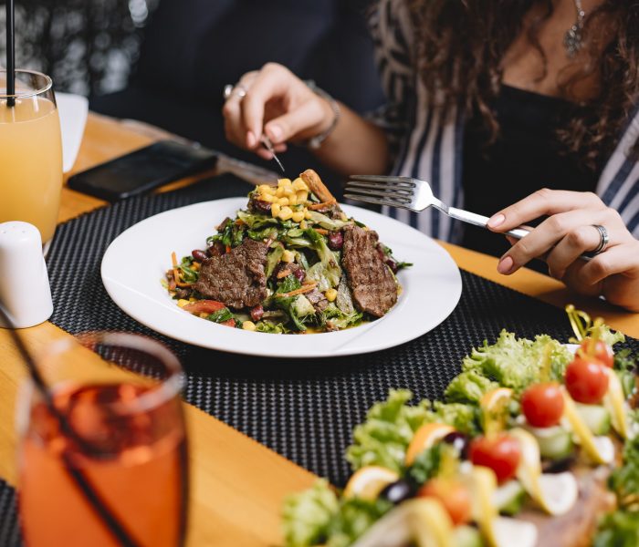 side view of a woman eating beef meat salad with vegetables and corns